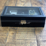 Une boîte de montre en cuir noir Boites Lefiguet sur une table en bois.
